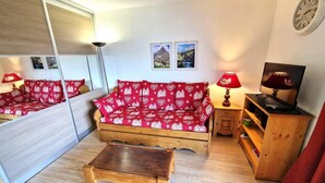 A cozy living room with a wooden sofa, a coffee table, a TV stand, and a mirror reflecting the room. - 30m from ski slopes, 3rd floor, view open, balcony, tv, ski locker, 42m², Valfréjus (Valfréjus)