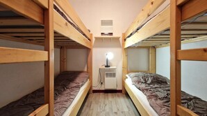 Et aflangt værelse med to køjesenge, et lille skrivebord med lampe og en varmeovn.