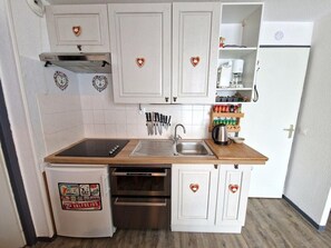 Uma cozinha compacta com armários brancos, pia de aço inoxidável e forno embutido.