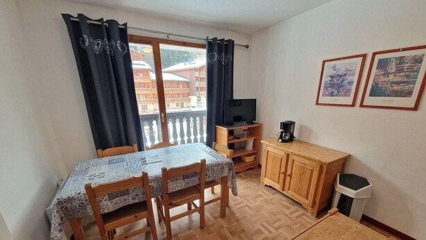 A small, cozy room with a wooden dining table and chairs, a wooden cabinet, a television, and a window with curtains. - 30m from ski slopes, 3rd floor, balcony, tv, ski locker, 32m², Valfréjus (Valfréjus)
