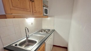Een compacte keuken met houten kastjes, een roestvrijstalen spoelbak, een magnetron en een vaatwasser.