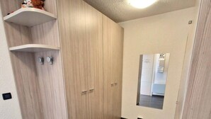 A room with a wooden wardrobe, a small shelf with toys, and a mirror on the wall.
