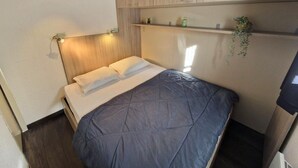 A compact bedroom with a bed, wooden headboard, built-in shelves, and a small plant.