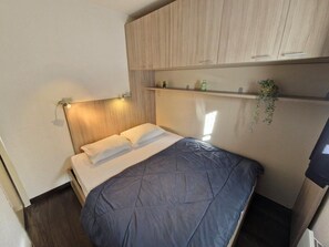 Ein gemütliches Schlafzimmer mit Bett, Holz-Kopfteil, eingebauten Regalen und einer kleinen Pflanze.