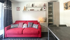 A cozy living room with a red sofa, a wooden coffee table, and a bookshelf with various decorative items.