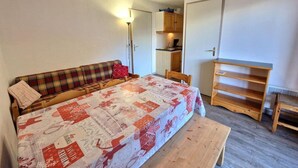 A bedroom with a bed, a wooden bench, a sofa, and a kitchenette. - 30m from ski slopes, 3rd floor, balcony, tv, ski locker, 32m², Valfréjus (Valfréjus)