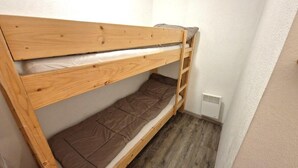A bunk bed with a wooden frame and brown mattress in a small room with white walls and a vent on the wall. - 30m from ski slopes, 3rd floor, balcony, tv, ski locker, 32m², Valfréjus (Valfréjus)