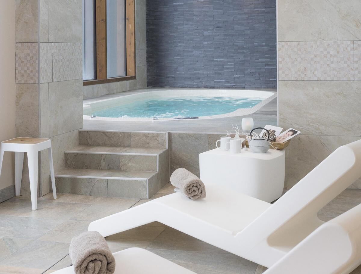 Un espace spa moderne doté d’un jacuzzi, de chaises longues blanches et d’un petit tabouret.