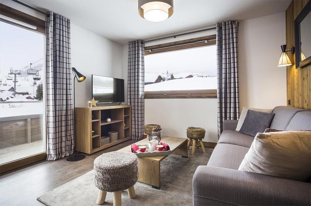 A modern living room with a sofa, a coffee table, a TV, and a view of a snowy landscape through large windows.