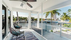 A balcony with a ceiling fan, two wicker chairs with cushions, a patterned rug, and a view of palm trees and a marina. - Serene Waterfront 2BR 2BA with Intracoastal Views, Pool, Balcony, Parking (Boca Raton)