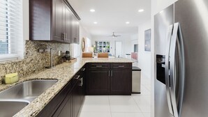 A modern kitchen with dark cabinets, granite countertops, stainless steel appliances, and a large island with seating. - Serene Waterfront 2BR 2BA with Intracoastal Views, Pool, Balcony, Parking (Boca Raton)