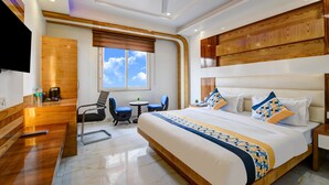 A hotel room with a large bed, a desk, two chairs, a small table, and a TV. - The York Legacy (New Delhi)