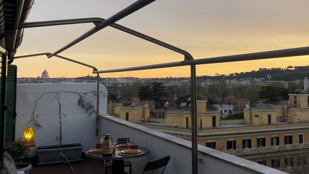 A balcony with a table and chairs, overlooking a cityscape with buildings and a dome structure in the distance. - Penthouse _ 70' Suite Gallery with Panoramic Terrace (Roma)