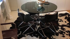 A dining area with a round glass table, black chairs, a chandelier, and a cowhide rug. - Penthouse _ 70' Suite Gallery with Panoramic Terrace (Roma)