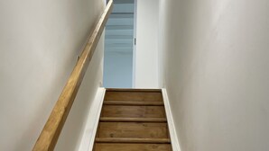 Un escalier en bois, avec des murs blancs et une main courante sur le côté gauche.