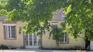 Une terrasse avec une table ronde et deux chaises, un mur en briques et une fenêtre avec des volets.