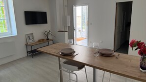 Une cuisine moderne avec un plan de travail en bois, deux tabourets de bar, une table à manger et un téléviseur fixé au mur.