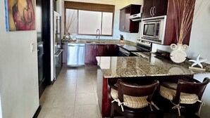 A modern kitchen with a granite countertop, dark wooden cabinets, a built-in microwave, and a dining area with three chairs. - 2-bedroom condo in Reserva Conchal, best ocean view!!! (Playa conchal)