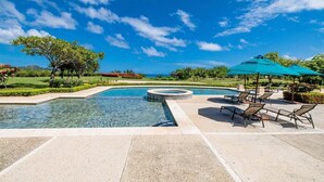 A swimming pool with lounge chairs and umbrellas, surrounded by well-manicured gardens and a clear blue sky. - 2-bedroom condo in Reserva Conchal, best ocean view!!! (Playa conchal)