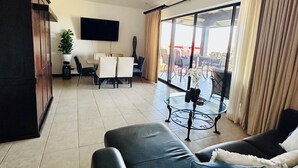 A spacious living room with a large black leather sofa, a glass coffee table, and a ceiling fan. There is a dining area with a table and chairs, and a balcony with outdoor furniture. - 2-bedroom condo in Reserva Conchal, best ocean view!!! (Playa conchal)