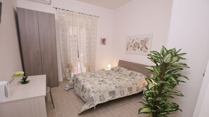 A bedroom with a bed, a bedside table, a potted plant, a curtain, and a wall-mounted artwork. - Rooms Monteverde (Rome)