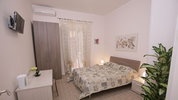 A bedroom with a bed, bedside table, lamp, potted plant, and a TV mounted on the wall. - Rooms Monteverde (Rome)