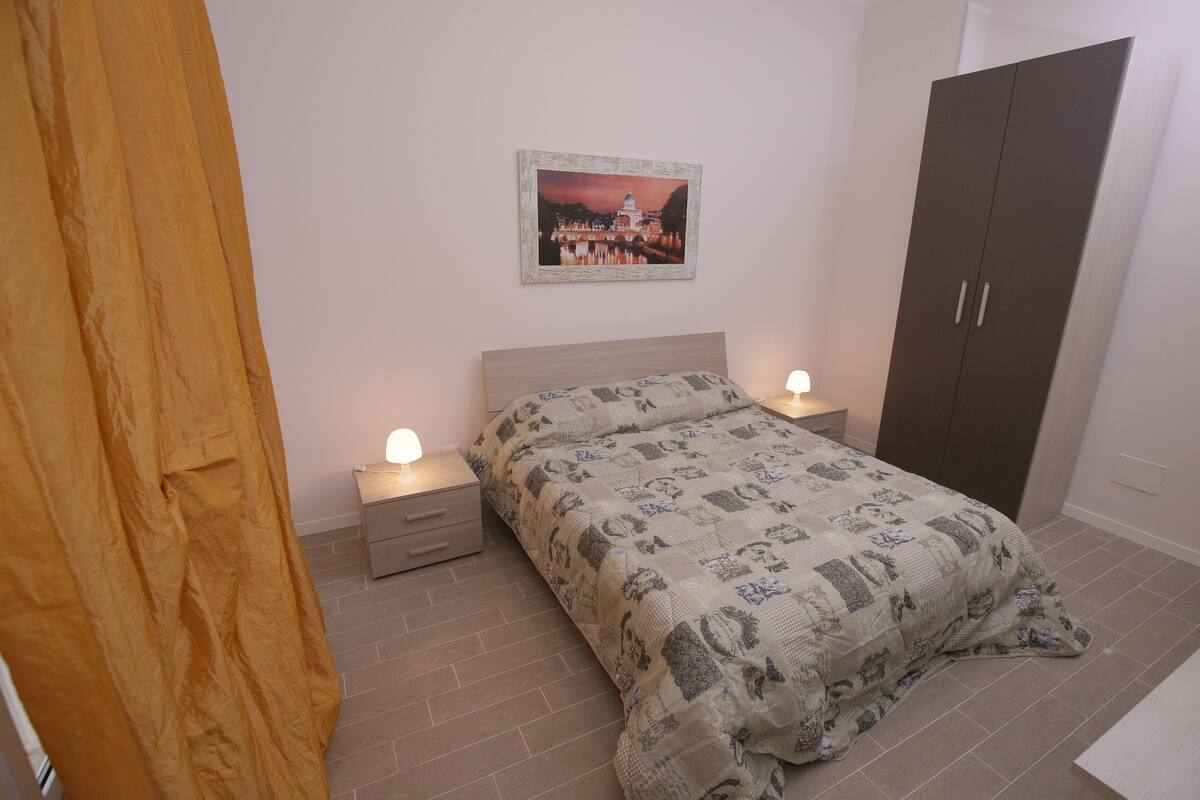 A bedroom with a bed, nightstands, a wardrobe, and a wall-mounted picture.