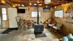 A cozy living room with a wooden interior, a sofa, a chair, a fireplace, and a TV mounted on the wall.
