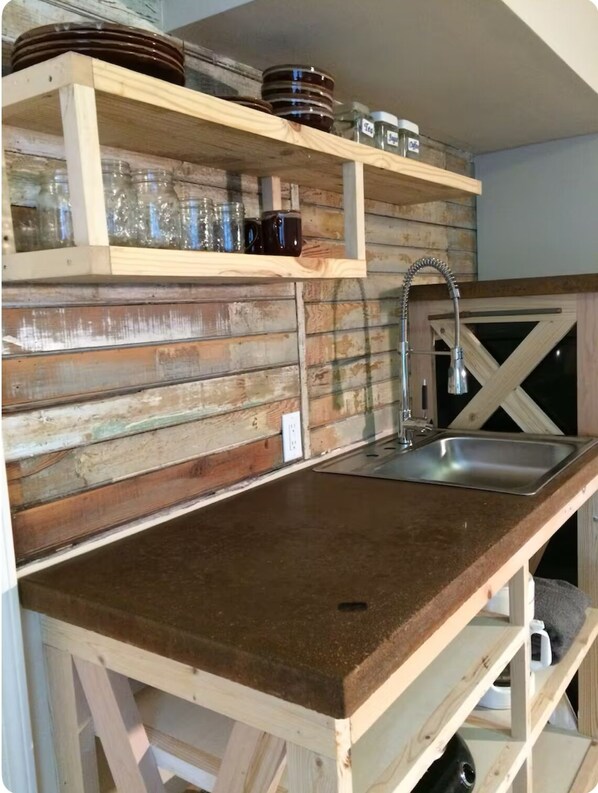 Una cocina rústica con estantes de madera, un lavamanos de acero inoxidable y una encimera de madera.