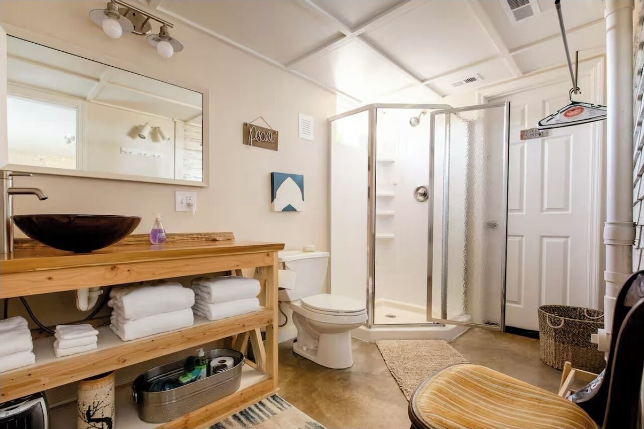 A bathroom with a wooden vanity, a large mirror, a glass shower enclosure, and a white toilet.
