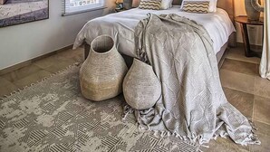 A bedroom with a sloped ceiling, a bed with patterned bedding, decorative wall art, and a large woven rug. - NEW LISTING: Hidden Pearl Luxurious Villa - Ocean View (Philipsburg)