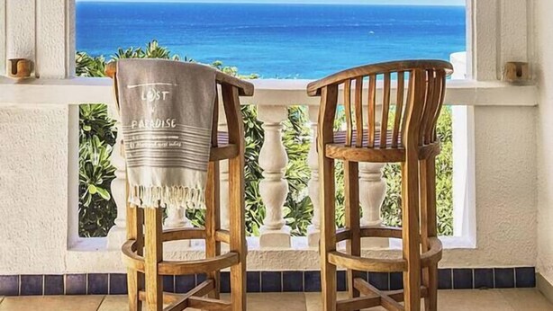 A balcony with two wooden chairs, a ceiling fan, and a view of the ocean. - NEW LISTING: Hidden Pearl Luxurious Villa - Ocean View (Philipsburg)