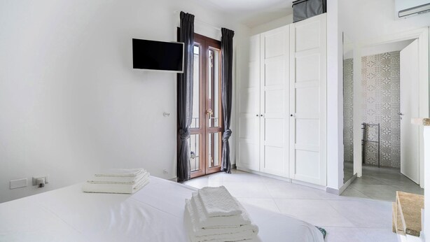 A bedroom with a bed, a TV mounted on the wall, a wardrobe, and a door leading to a bathroom.