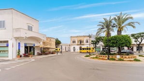 A street with buildings, a yellow bus, and palm trees.