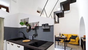 A compact kitchen with a black countertop, a sink, and a stove. There is a dining area with a yellow sofa and a small table.
