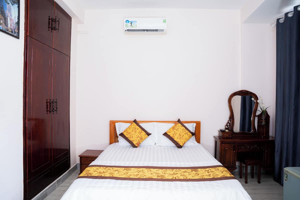 Ein Hotelzimmer mit einem großen Bett, einem Kleiderschrank, einem Schreibtisch mit Spiegel und einer Klimaanlage an der Wand.