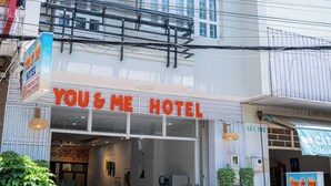 A two-story hotel with a sign reading "You & Me Hotel". There are two scooters parked in front, and the entrance has a sign indicating room rates.
