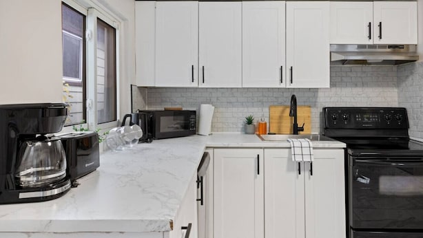A kitchen with white cabinets, a black stove, a microwave, and a coffee maker. - Walkerville 1BR Suite Near Caesars Windsor | RiverWalk, Waterfront & Downtown (Windsor)