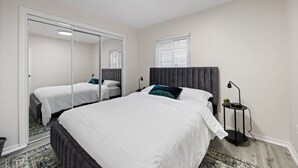 A bedroom with a large bed, a wardrobe with a mirror, a bedside table with a lamp, and a window with blinds. - Walkerville 1BR Suite Near Caesars Windsor | RiverWalk, Waterfront & Downtown (Windsor)