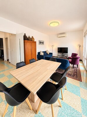 Una sala de estar moderna con una mesa de comedor de madera, sillas negras, un sofá azul y un sillón púrpura.