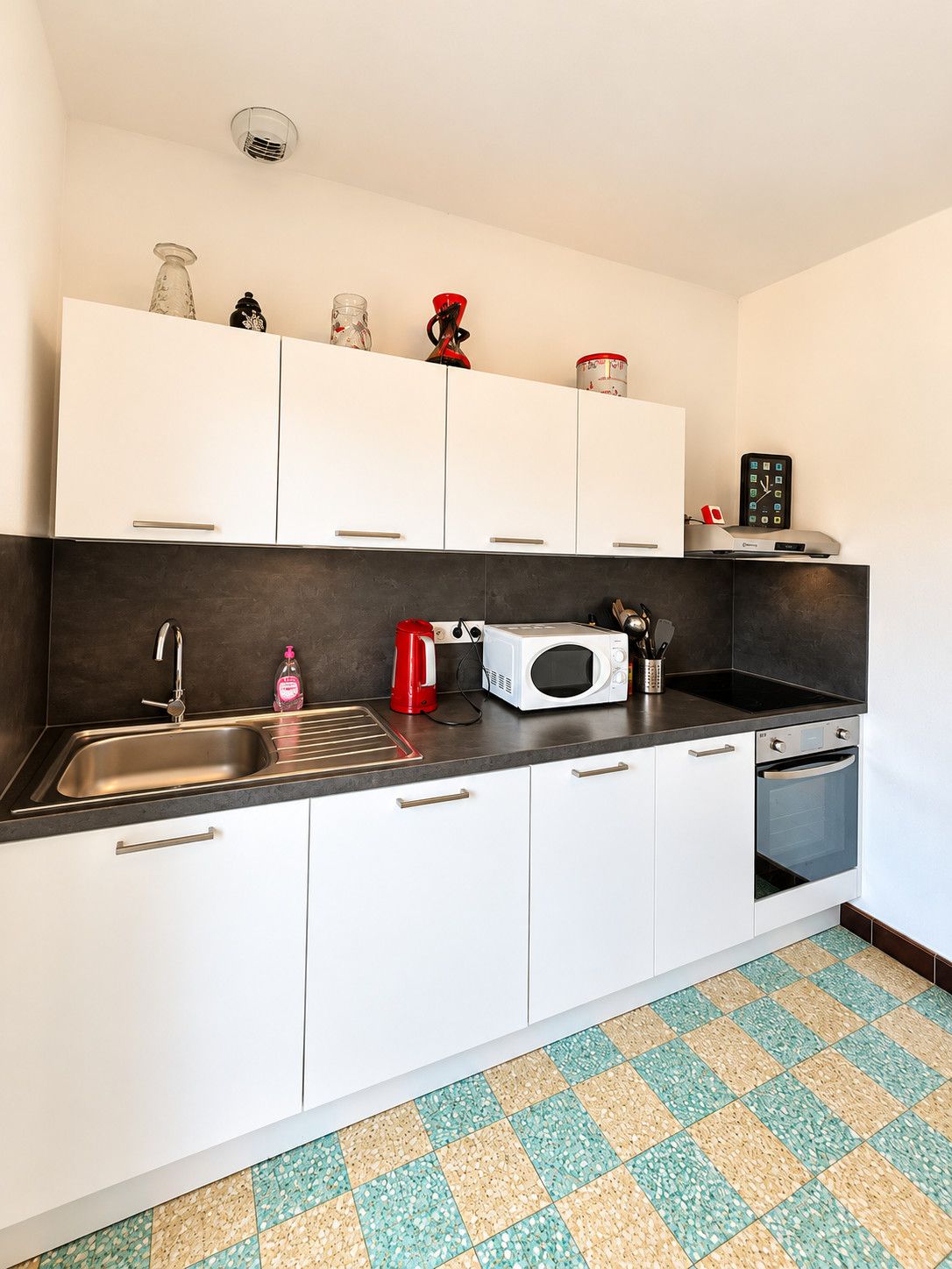 Eine kompakte Küche mit weißen Schränken, einer Edelstahl-Spüle, einer Mikrowelle und einem kleinen Backofen.