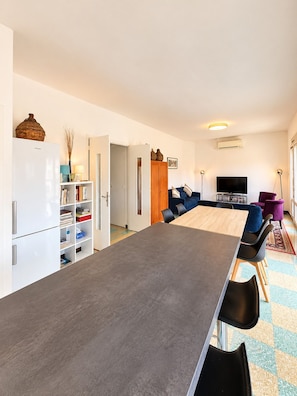 A modern living room with a dining area, a television, and a bookshelf.