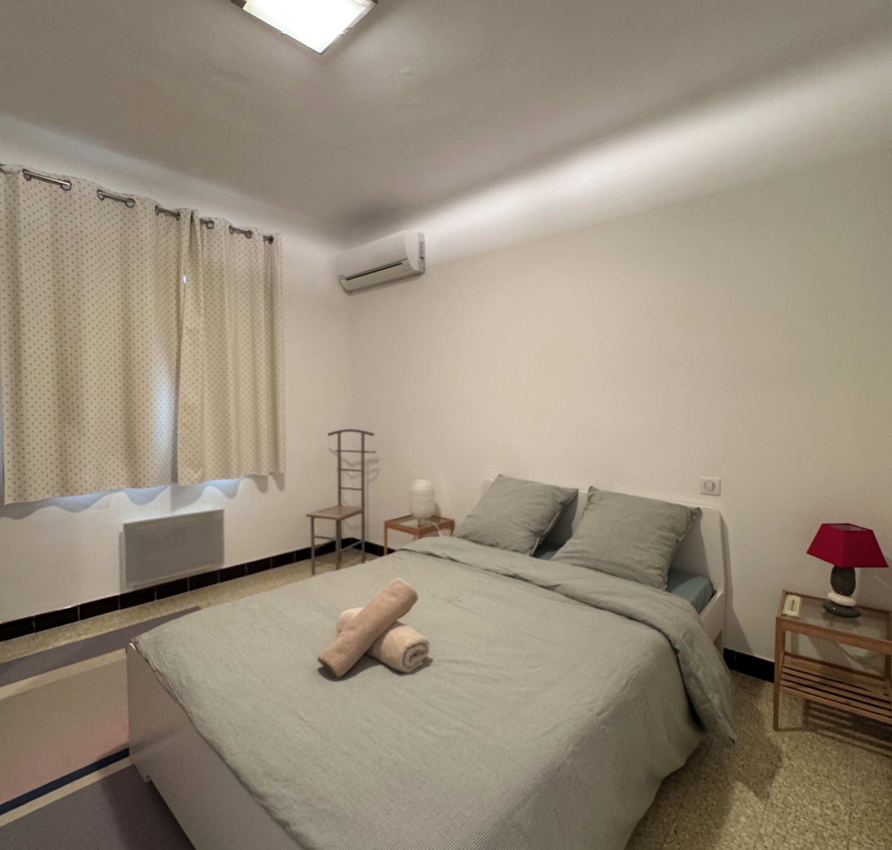 Quarto com cama, uma cadeira, mesa de cabeceira e ar condicionado.