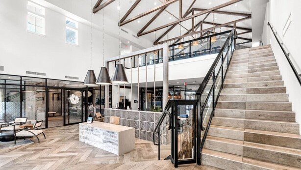 A spacious lobby with a wooden staircase, a reception desk, and hanging pendant lights.