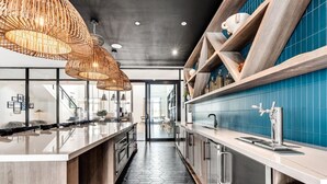 A modern kitchen with a long island, pendant lights, and a blue tiled backsplash.
