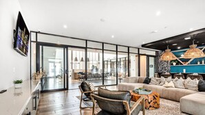 A modern living room with a sofa, coffee table, and chairs. There is a kitchen area in the background with a dining table and chairs.