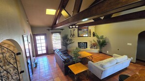 Een ruime woonkamer met een open haard, een bank, een eettafel en een groot raam.