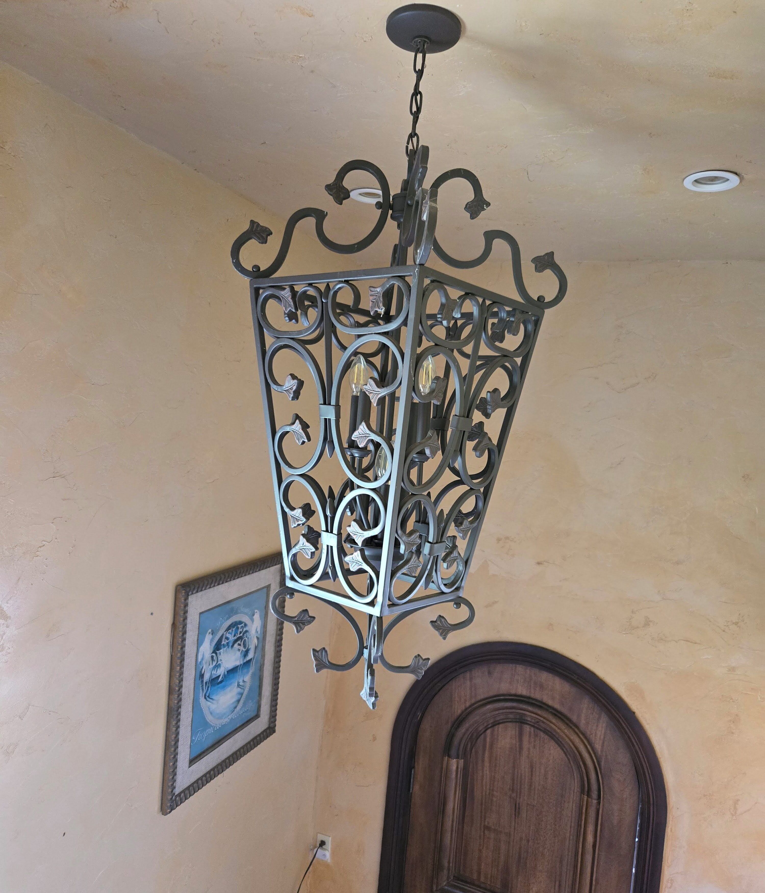Ein Zimmer mit einem dekorativen Metallkronleuchter, einem gerahmten Bild an der Wand und einer Holztür.