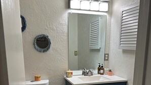 Et badeværelse med et hvidt toilet, en blå kommode med spejl og en pink måtte.
