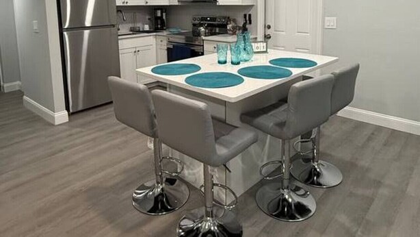 Una cocina moderna con armarios blancos, un refrigerador de acero inoxidable y una isla central con taburetes de bar.